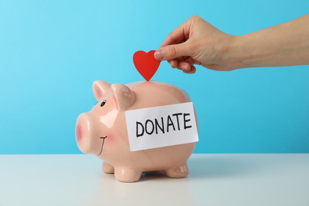 Female hand puts heart in piggy bank with text Donate against blue background