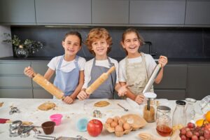 Happy children with wooden and metal rolling pins making cookies